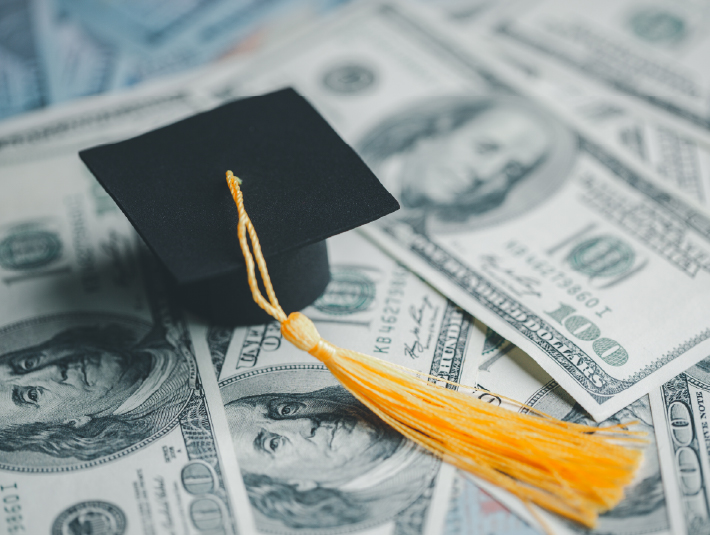 graduation cap on top of stacks of hundred dollar bills