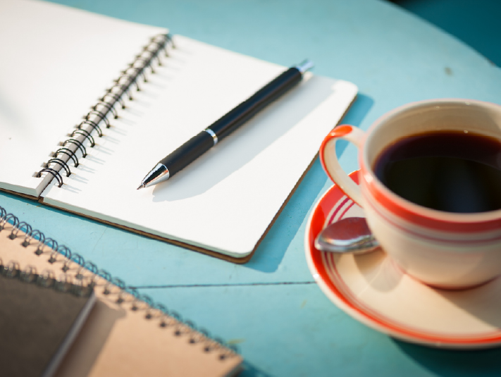 cup of tea next to a journal and pen on a desk